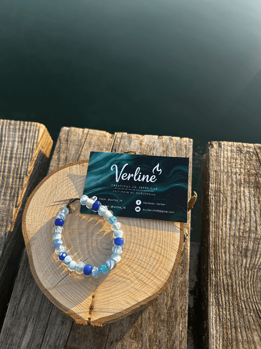 Bracelet en perles de verre aux nuances bleues posé sur un rondin de bois près de l'eau