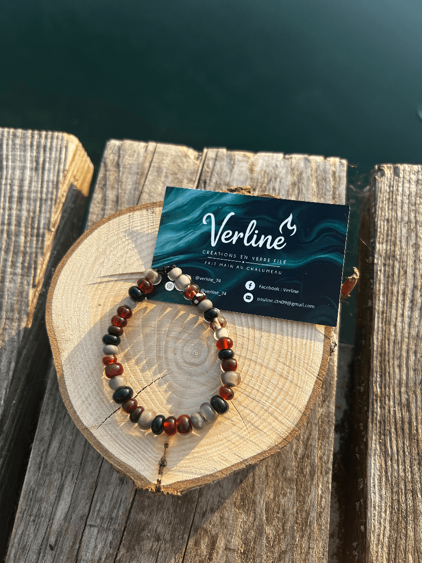 Bracelet en perles rondes ambre, noires et gris taupe posé sur une tranche de bois au bord de l'eau