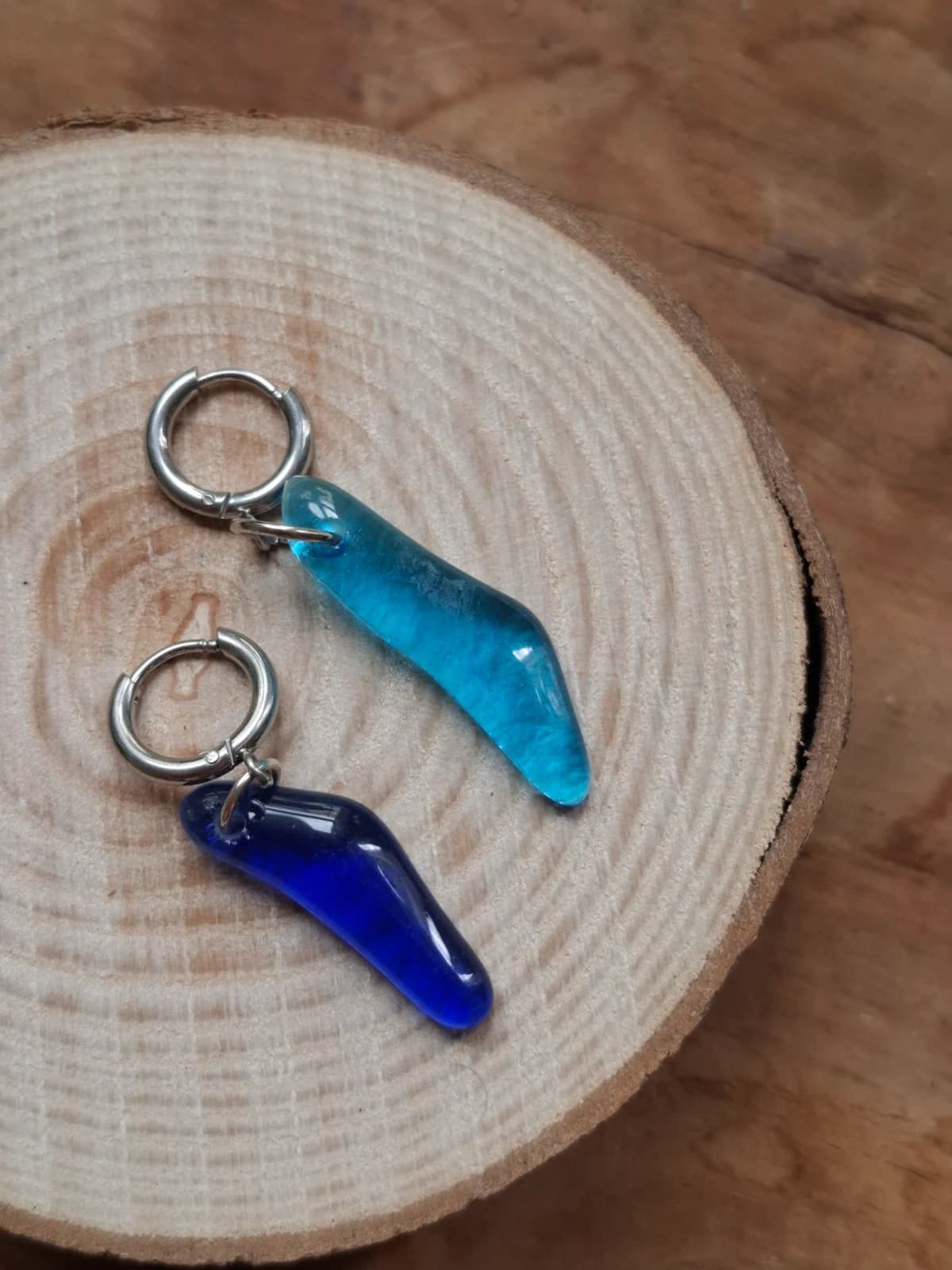 Boucles d'oreilles pendantes en verre bleu clair et bleu roi posées sur un disque de bois.