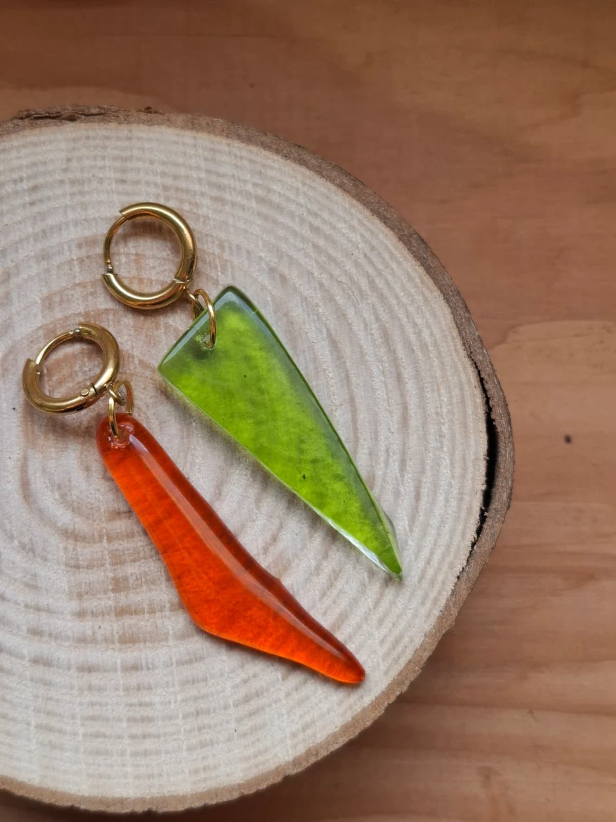 Boucles d'oreilles pendantes vert et orange suspendues sur un présentoir doré devant une fenêtre