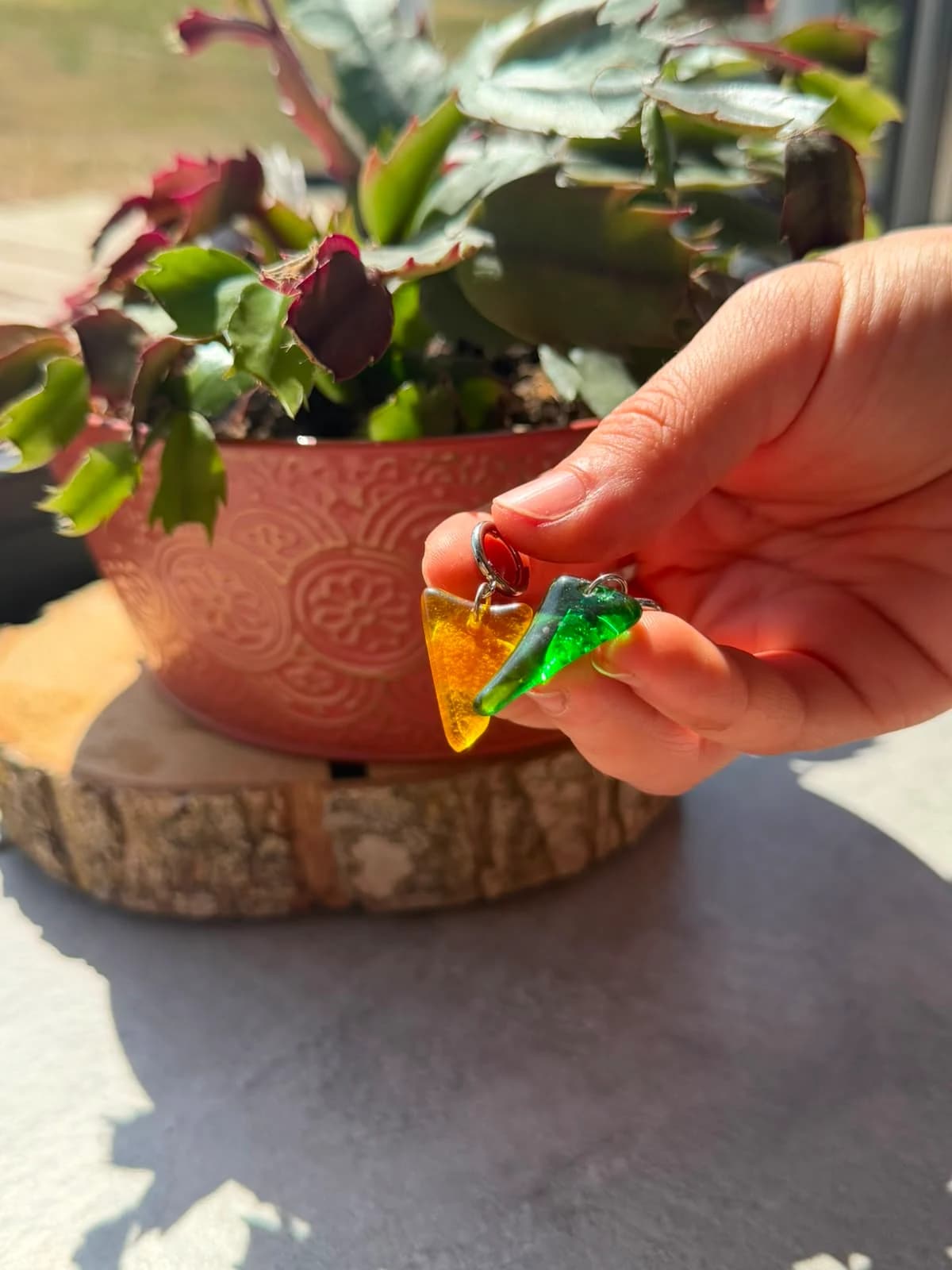 Boucles d'oreilles dormeuses avec pendentifs triangulaires en verre vert et jaune sur une tranche de bois.