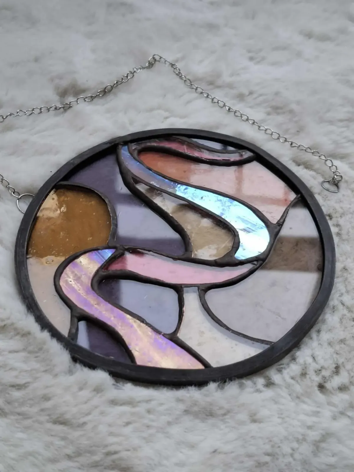 Vitrail rond Tiffany aux reflets holographiques roses et violets posé à plat sur un tissu doux