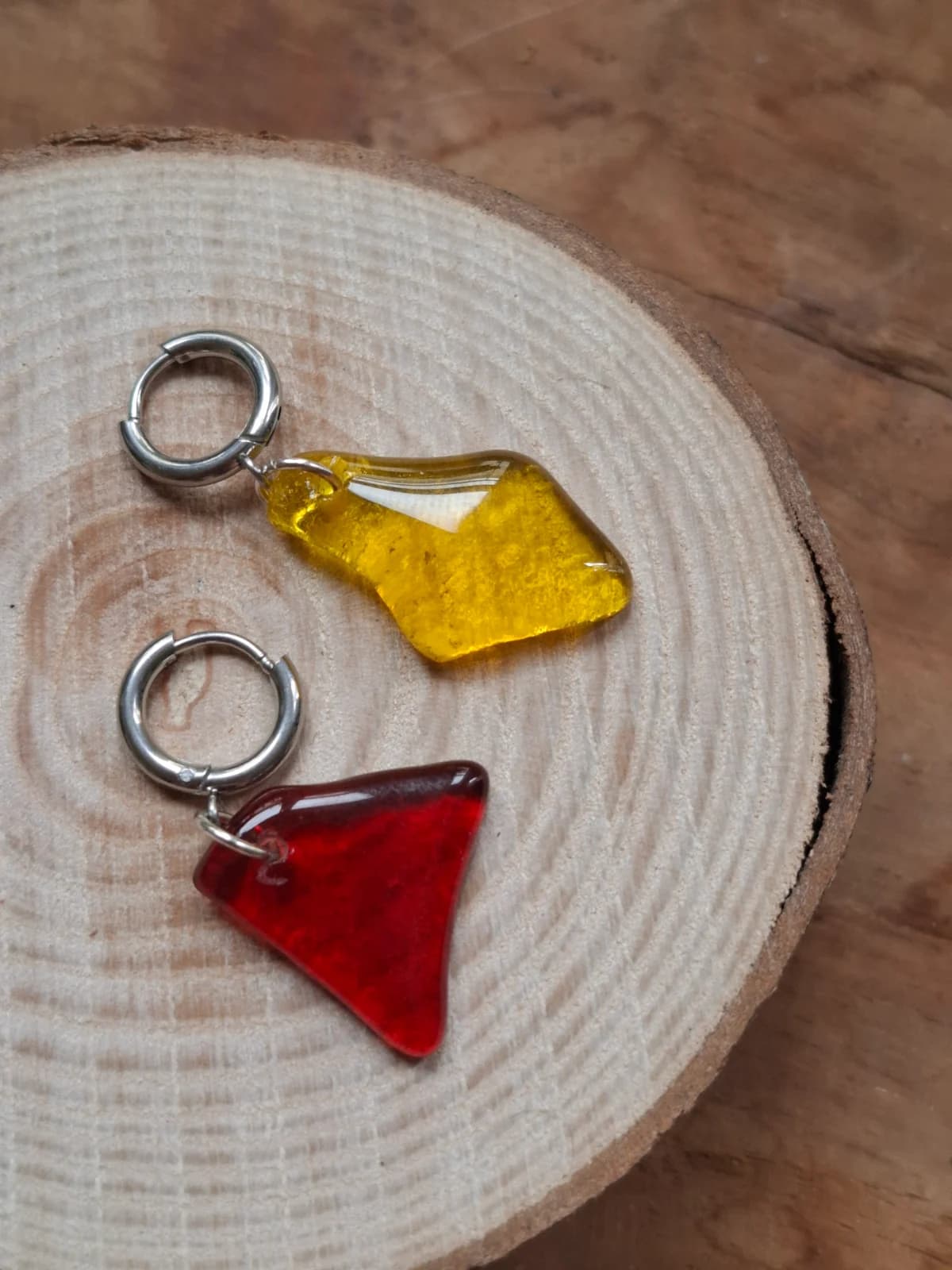 Boucles d'oreilles asymétriques en verre translucide rouge et jaune posées sur un rondin de bois
