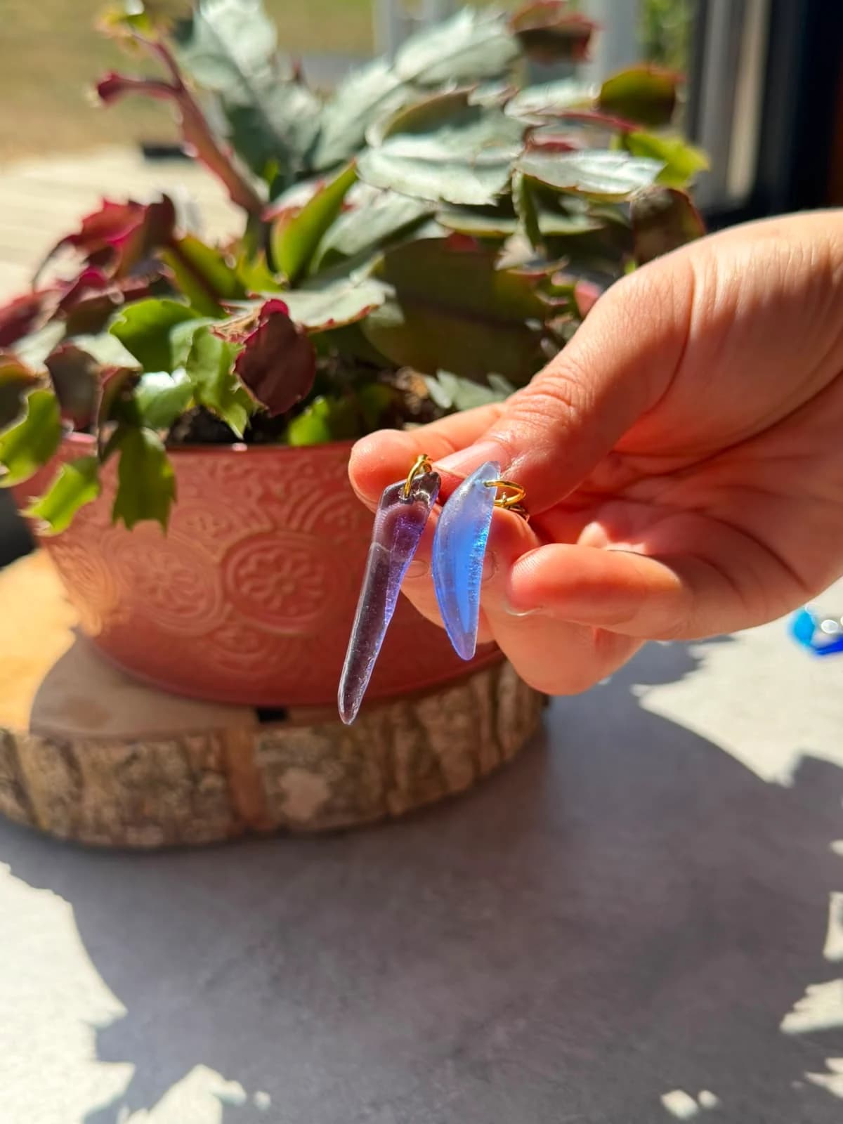 Paire de boucles d'oreilles asymétriques en verre translucide violet et bleu tenue en main à la lumière
