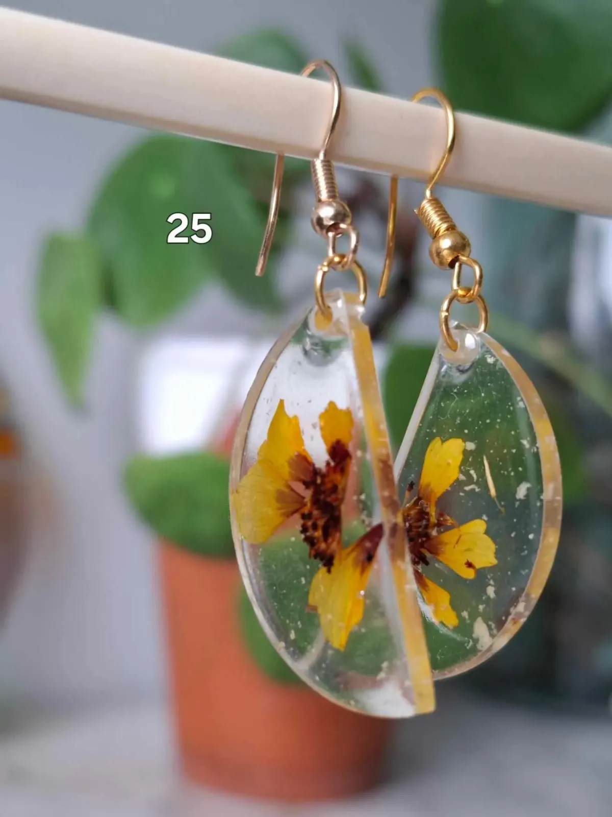 Boucles d'oreilles pendantes en résine transparente abritant des fleurs séchées jaunes sur crochets dorés.