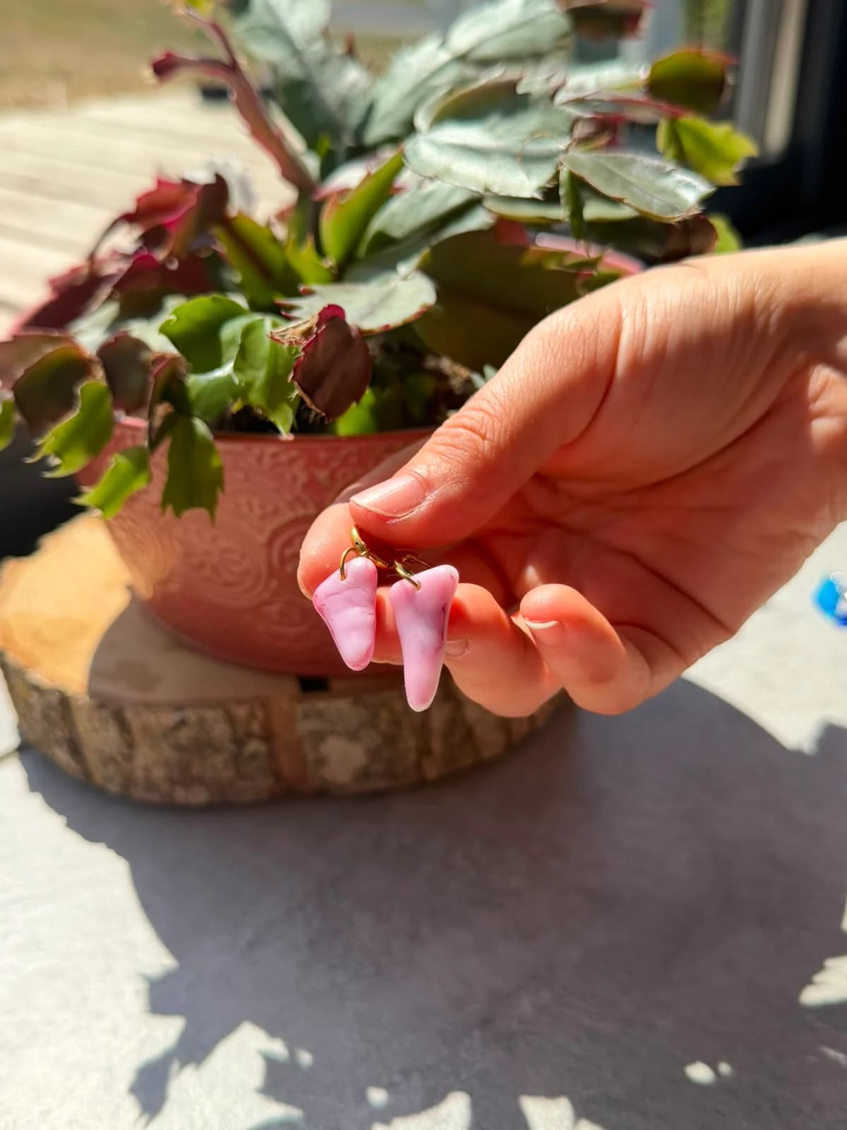 Boucles d'oreilles pendantes en verre rose tenues en main devant une plante en pot.