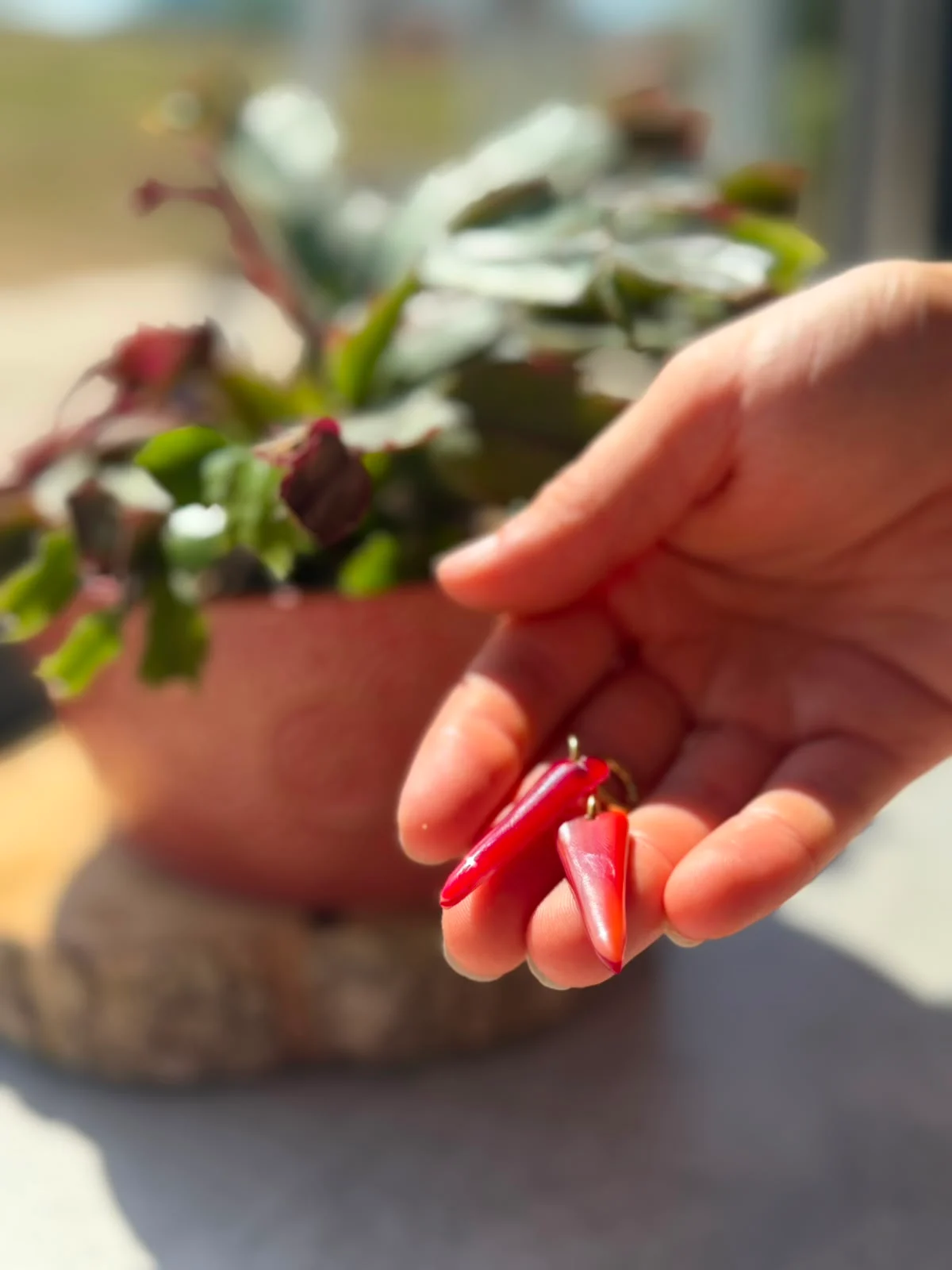 Paire de boucles d'oreilles en verre rouge allongées, tenues au creux d'une main devant une plante verte.