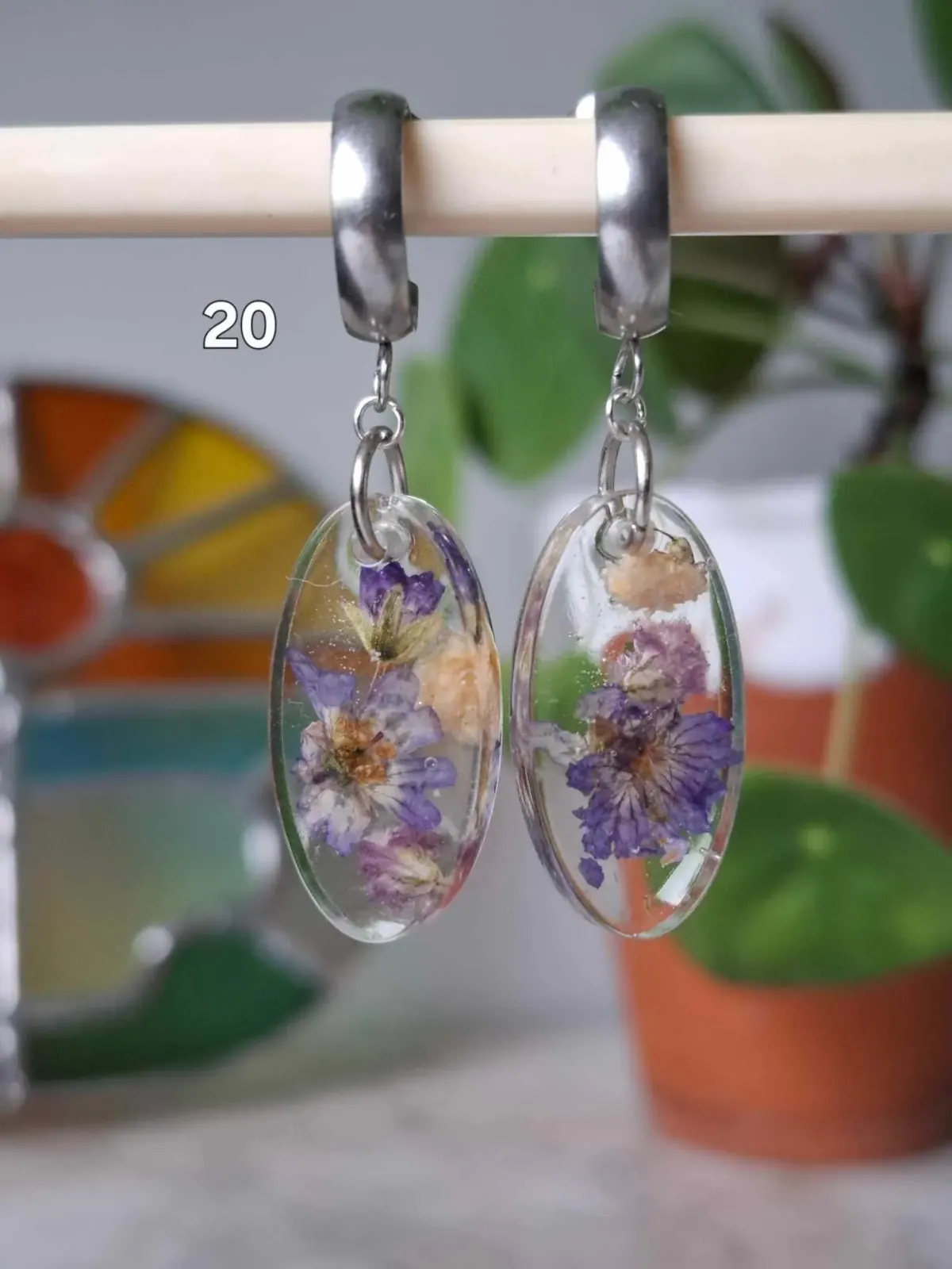 Boucles d'oreilles pendantes ovales en résine transparente avec inclusions de fleurs séchées violettes.
