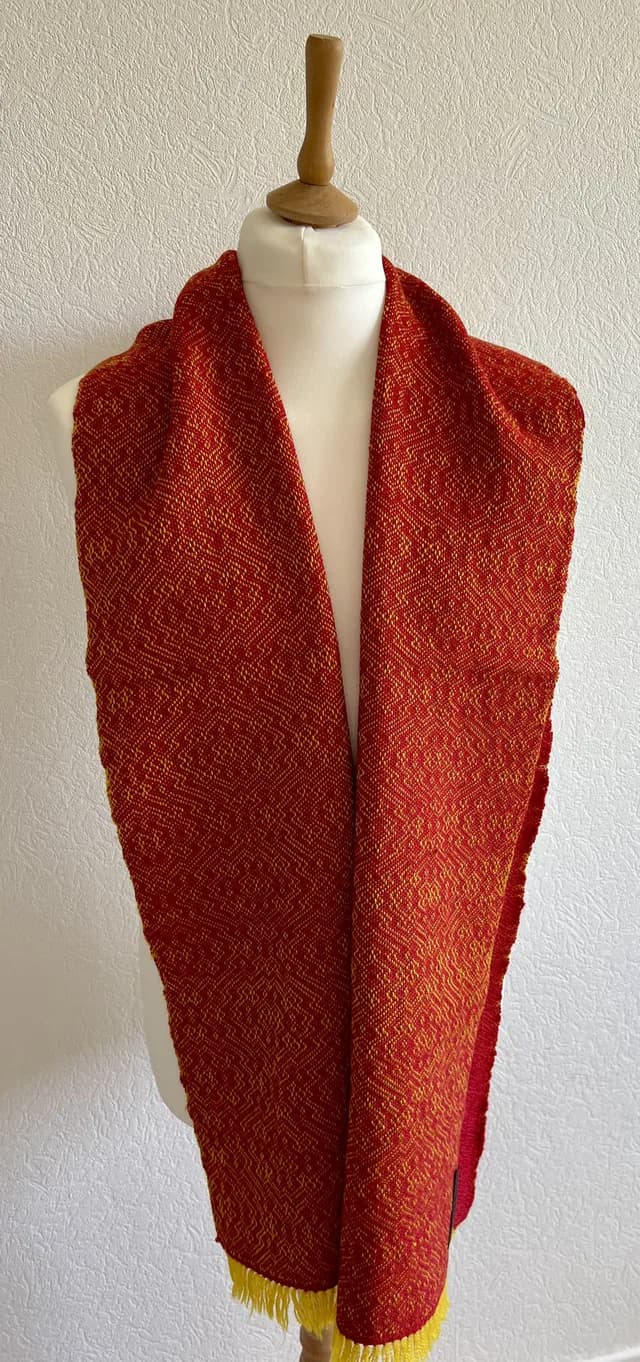 Écharpe tissée rouge et jaune à motifs géométriques et franges, drapée sur un buste de couture