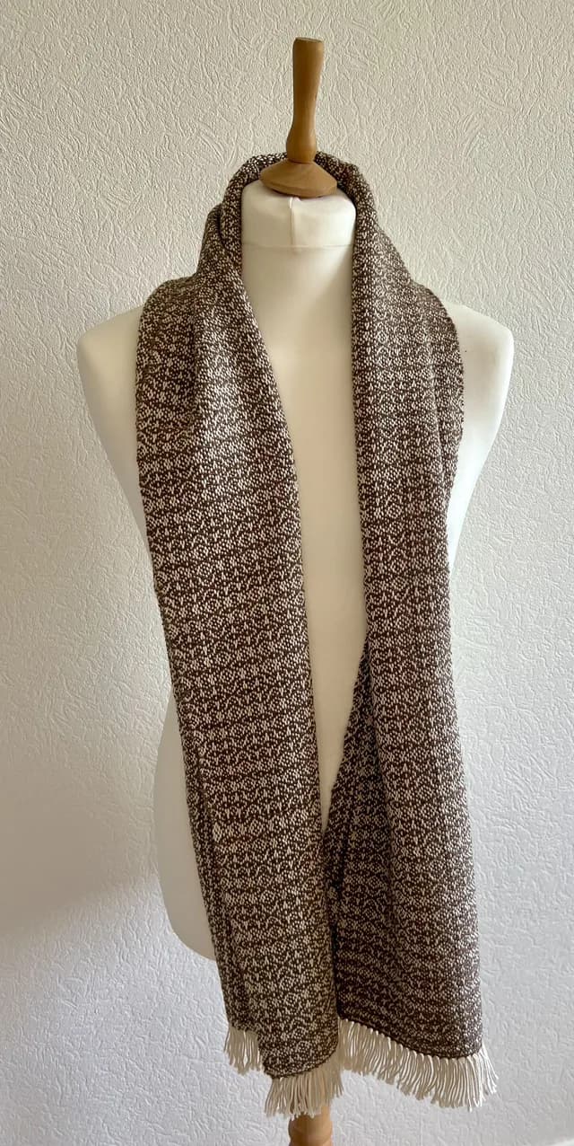 Écharpe tissée marron et blanche à franges portée sur un buste de couture blanc.
