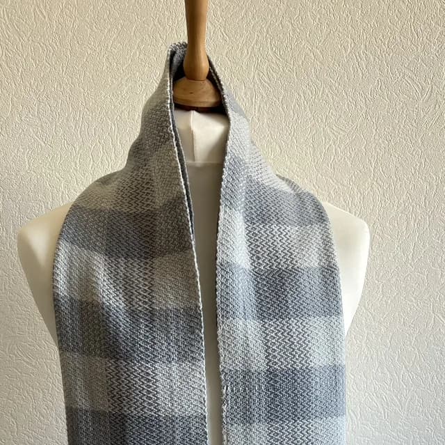 Écharpe tissée à carreaux blancs et gris drapée sur un buste de mannequin