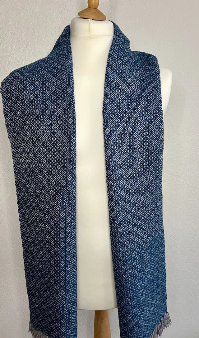 Écharpe tissée bleue et grise à motifs géométriques drapée sur un buste de mannequin