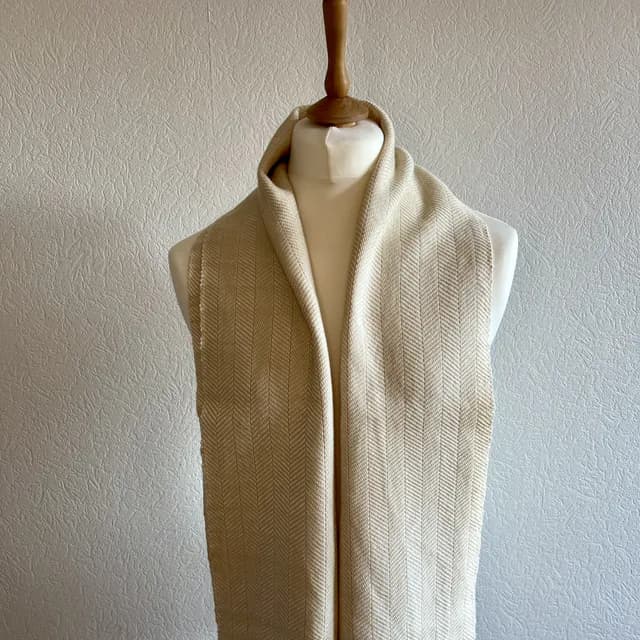 Écharpe tissée beige champagne et blanche à motifs chevrons portée sur un buste de mannequin blanc.