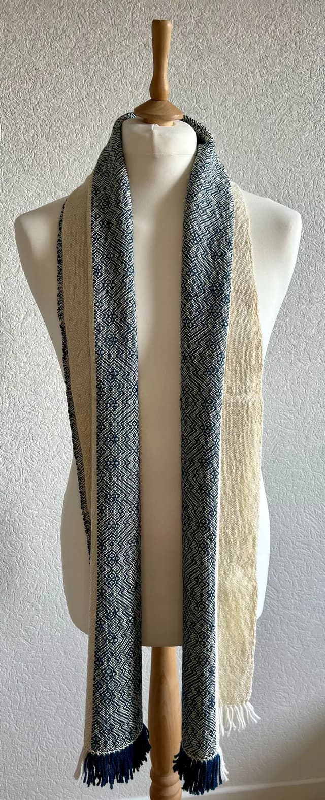Écharpe bicolore bleu et crème à motifs géométriques et franges, drapée sur un buste de mannequin.