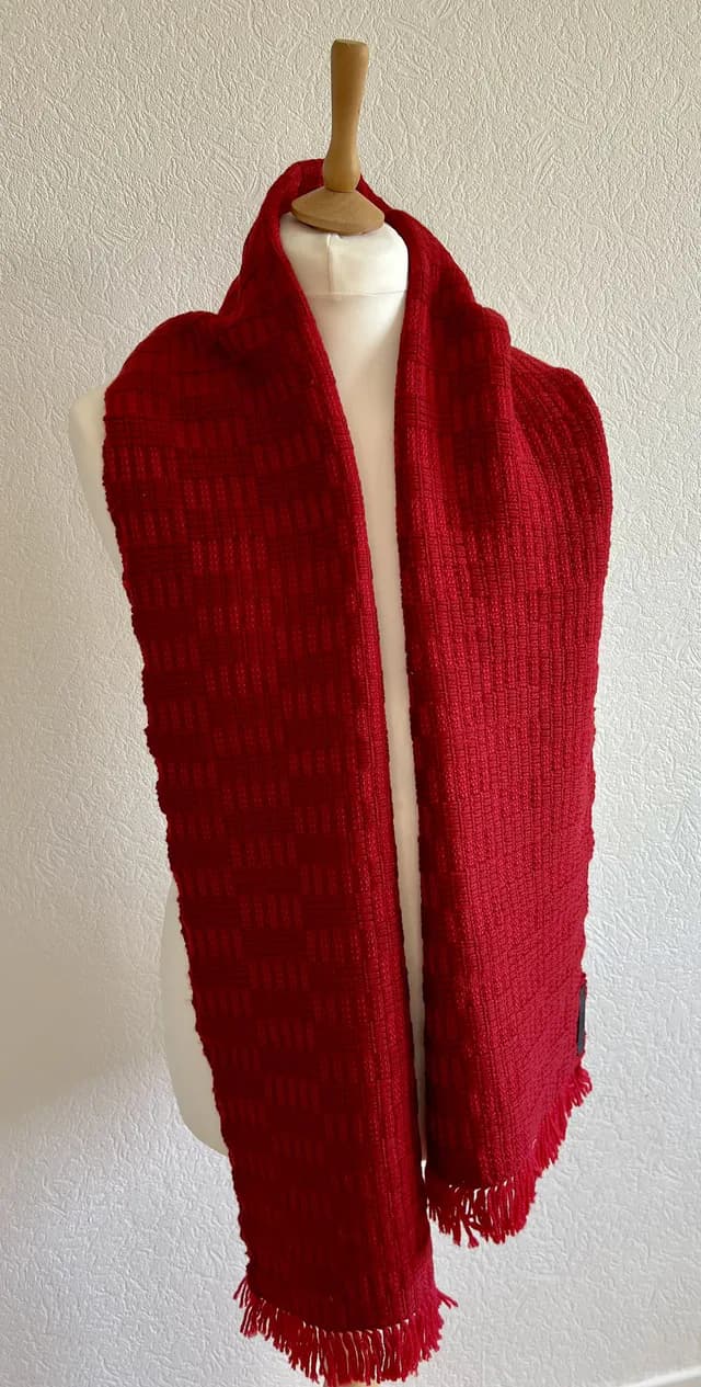 Écharpe rouge tissée main à franges portée sur un buste de mannequin blanc.