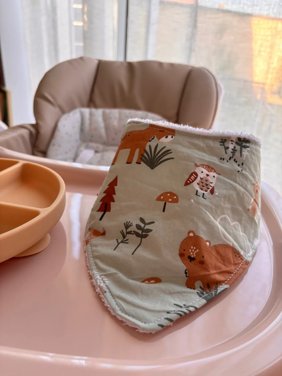 Bavoir bandana vert à motifs d'animaux de la forêt posé sur la tablette d'une chaise haute pour bébé.