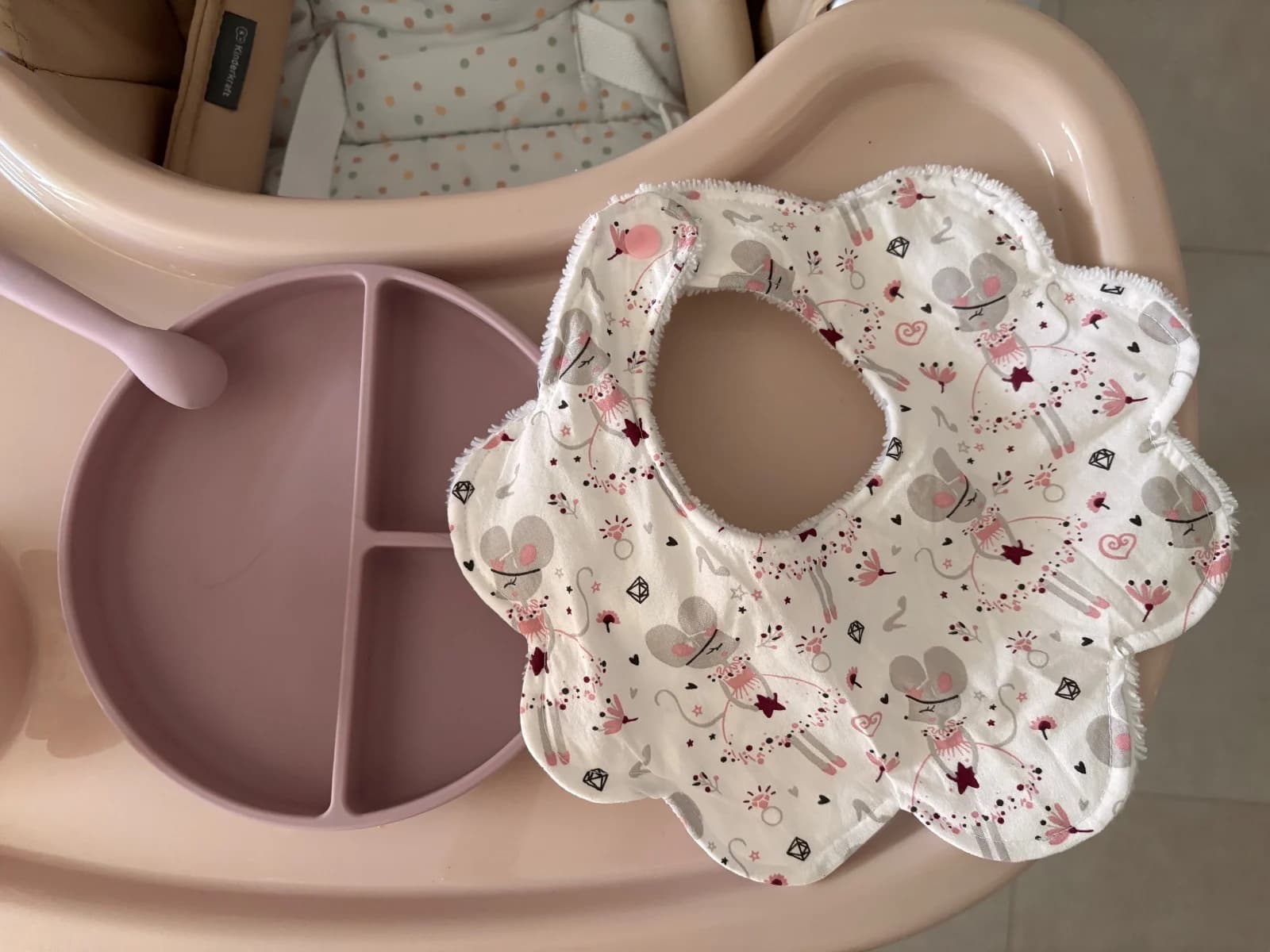 Bavoir collerette à motifs de souris ballerines posé sur un plateau de chaise haute à côté d'une assiette.
