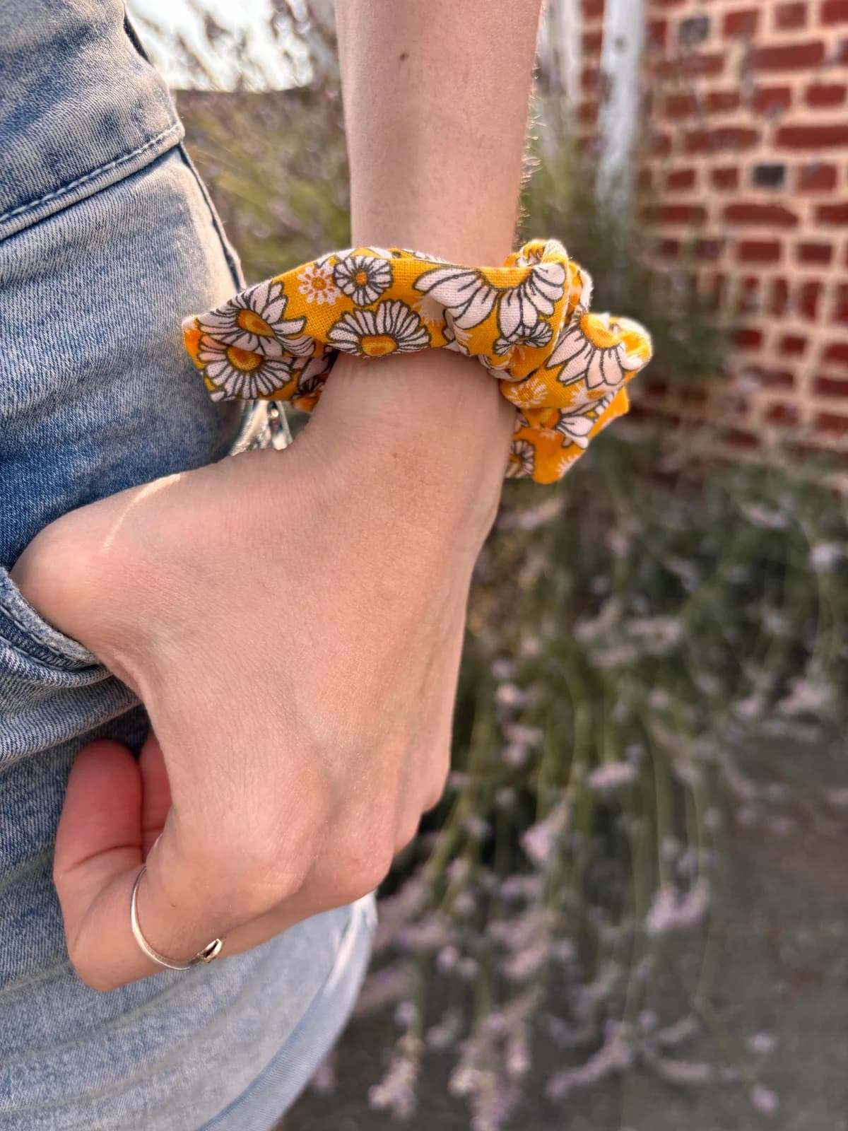 Chouchou jaune à motifs de marguerites porté au poignet, main glissée dans une poche en jean