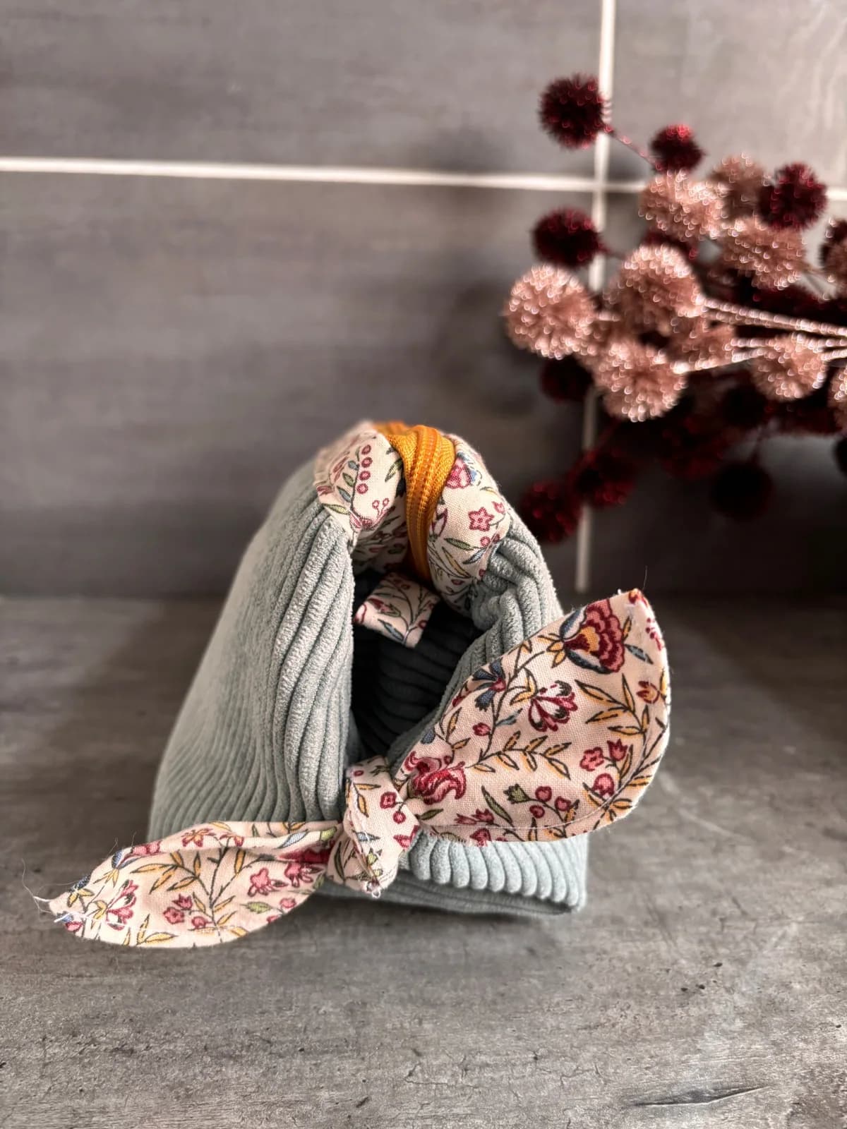 Trousse en velours côtelé vert d'eau fermée avec nœud fleuri sur le côté.