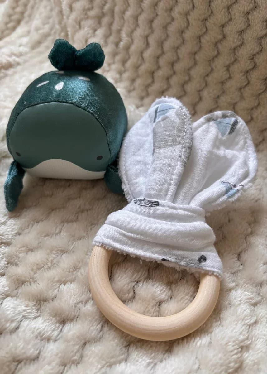 Anneau de dentition en bois avec oreilles en tissu Horizon céleste aux côtés d'une peluche baleine