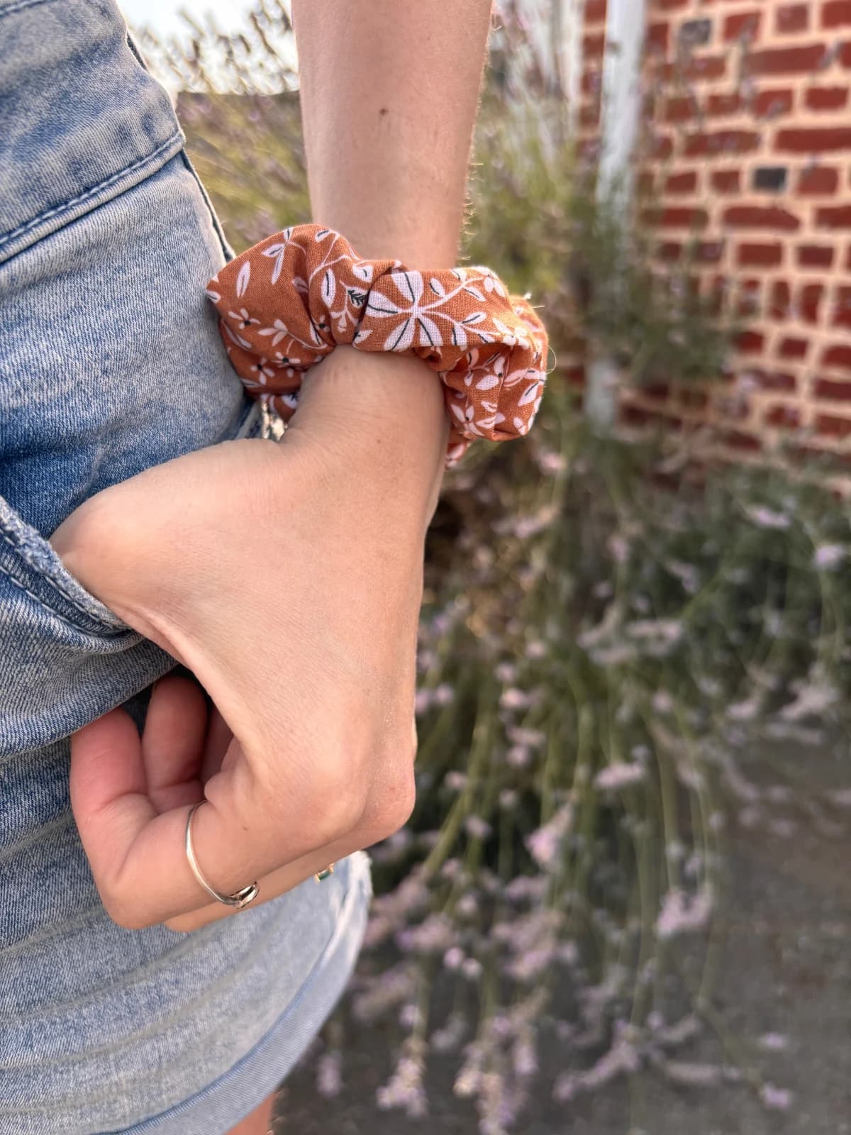 Chouchou en tissu marron cannelle à motifs floraux blancs, porté au poignet d'une personne.