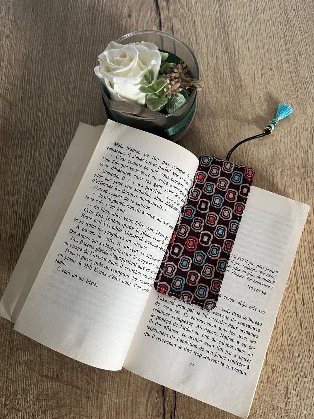 Marque-page en tissu à motifs géométriques rétro et pompon turquoise posé dans un livre ouvert