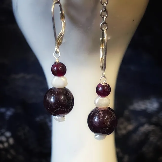 Gros plan sur des boucles d'oreilles pendantes avec perles de grenat bordeaux et perles blanches.