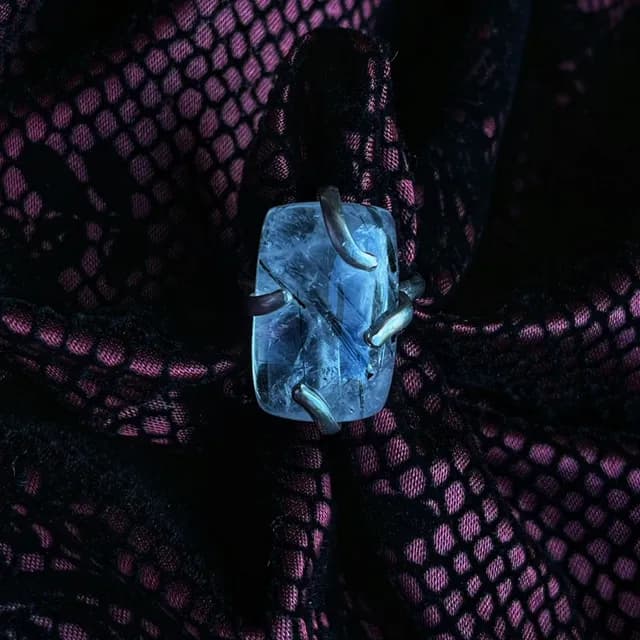 Bague en argent ornée d'un quartz rectangulaire à inclusions noires, posée sur un tissu texturé.