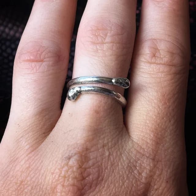 Bague ouverte argentée en forme d'allumette enroulée autour d'un doigt, vue rapprochée.