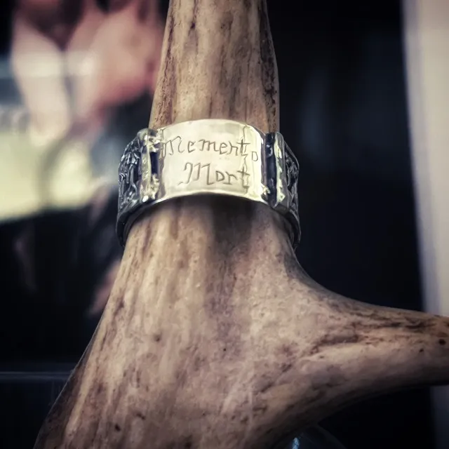 Bague large en argent gravée Memento Mori présentée sur un bois de cerf.