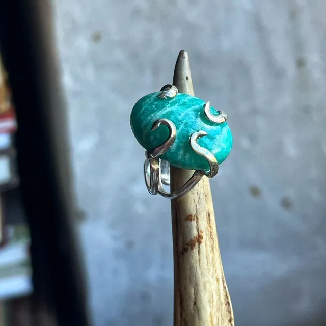 Bague en argent avec pierre ovale turquoise amazonite sertie de griffes en volutes sur support.
