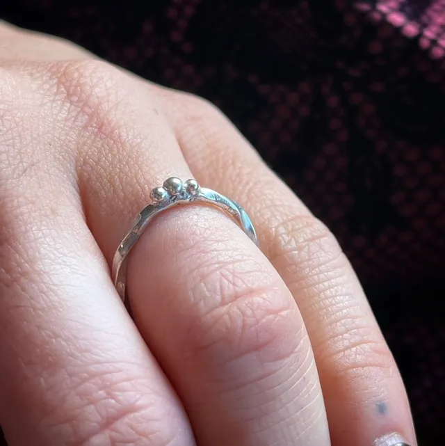 Bague fine en argent à motif torsadé surmontée de trois petites billes, portée à la main.