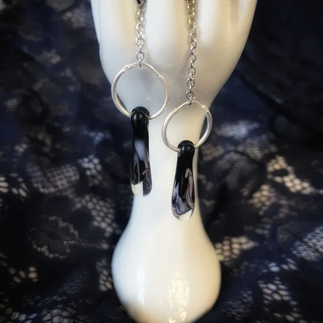 Créoles en argent ornées de gouttes en verre noir et transparent sur une main en porcelaine
