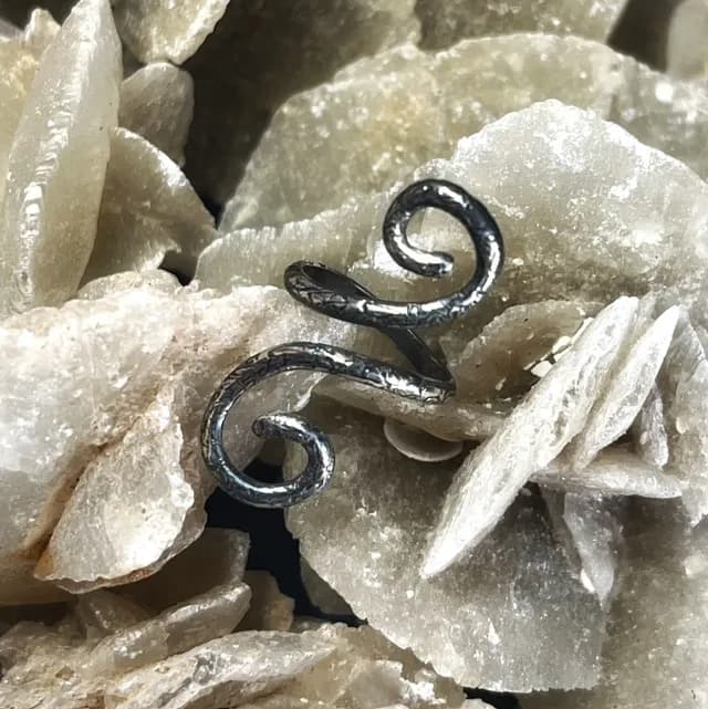Bague de phalange en argent 925 aux extrémités en volutes texturées, posée sur une pierre minérale.