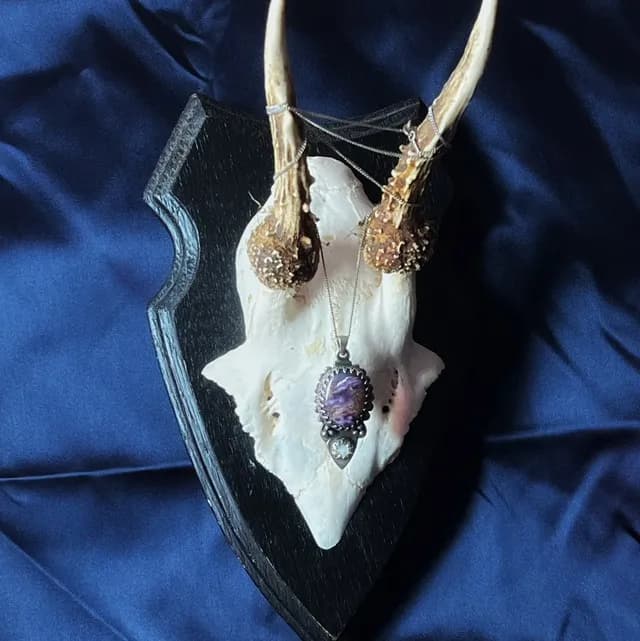 Pendentif artisanal orné d'une pierre violette suspendu à des bois de chevreuil sur fond bleu