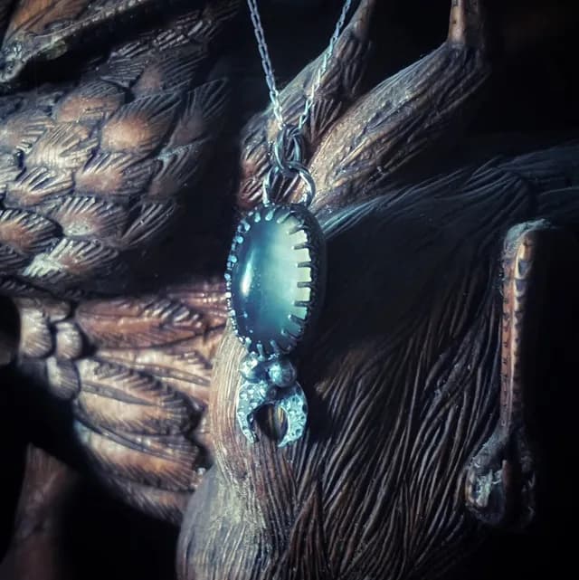 Pendentif en argent serti d'une pierre grise ovale surmontant un motif de croissant de lune texturé.