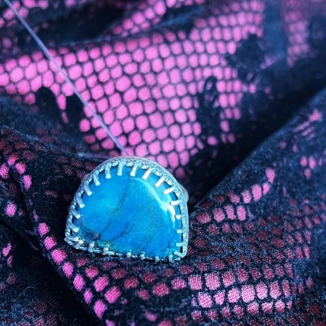 Bague en argent ornée d'une pierre demi-lune bleue turquoise posée sur un tissu texturé.