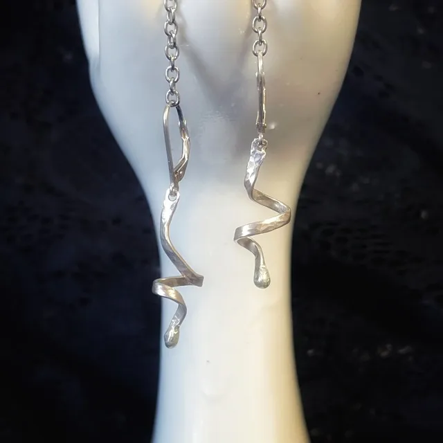 Gros plan sur deux boucles d'oreilles pendantes en spirale argentée suspendues à un support blanc