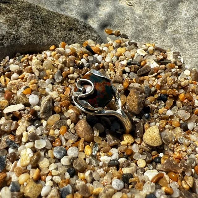 Bague en argent ornée d'un jaspe océan aux tons vert et brun, posée de trois-quarts sur des graviers