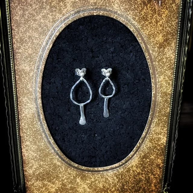 Paire de boucles d'oreilles pendantes en argent sur fond noir texturé dans un cadre doré ovale.