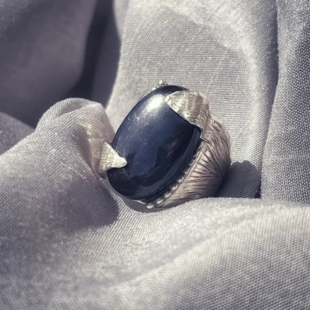 Bague en argent gravé ornée d'une pierre ovale sombre sur tissu gris drapé