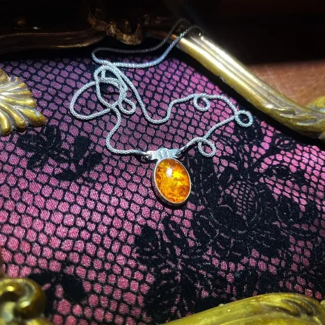 Collier en argent avec pendentif cabochon d'ambre doré posé dans un cadre doré sur dentelle.