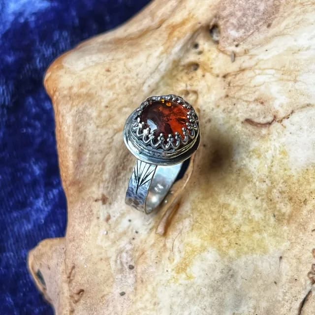 Bague en argent ciselé ornée d'une pierre d'ambre ronde sur fond texturé beige et velours bleu.