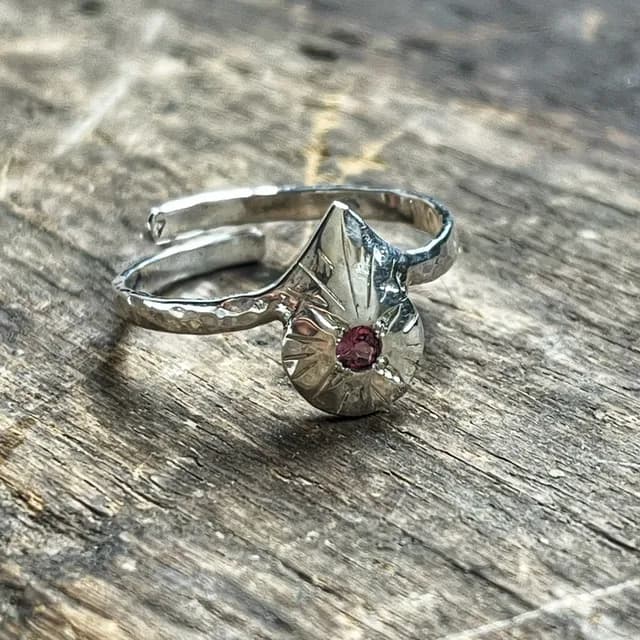 Bague réglable en argent martelé ornée d'un motif gravé et d'une pierre rose, posée sur du bois.