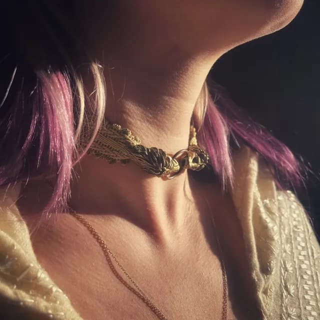Collier ras de cou en galon tissé doré et têtes de lions en laiton porté au cou.