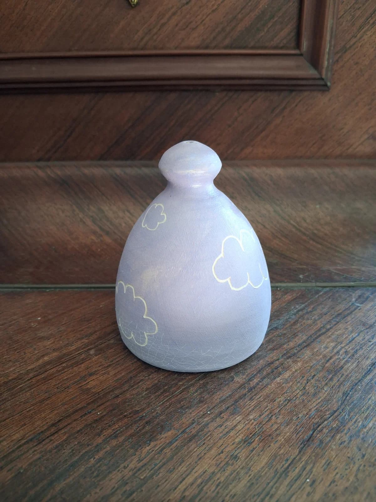 Arrosoir-main en céramique mauve clair orné de motifs de nuages blancs, posé sur un meuble en bois.