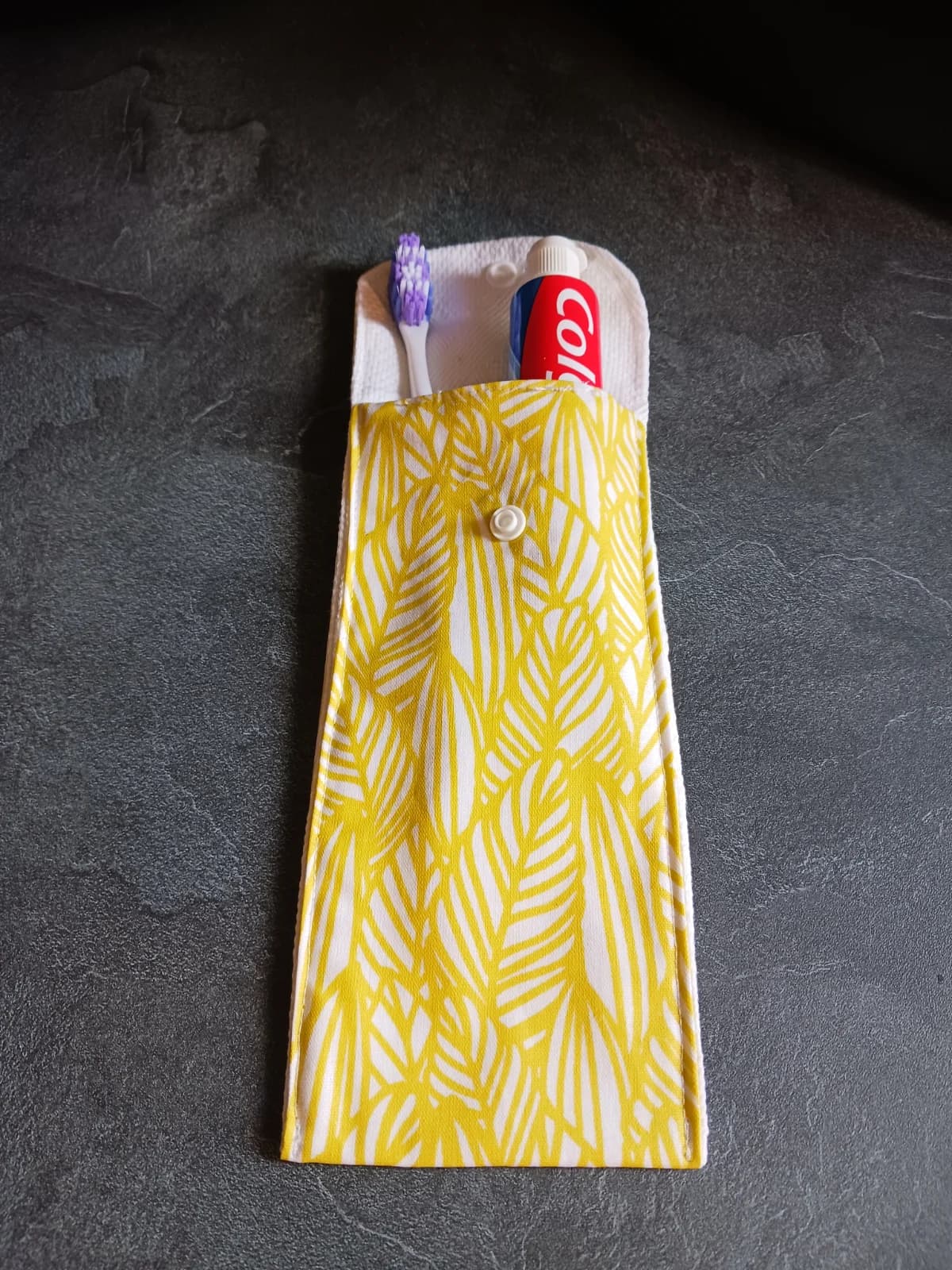 Étui en tissu ouvert à motif végétal jaune et blanc contenant une brosse à dents et un dentifrice.