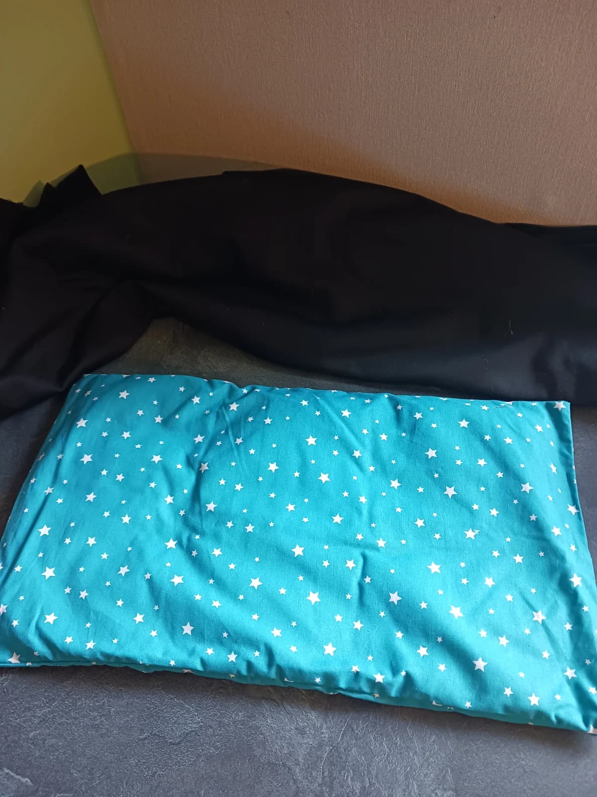 Bouillotte coussin rectangulaire dans sa housse turquoise ornée d'étoiles blanches.