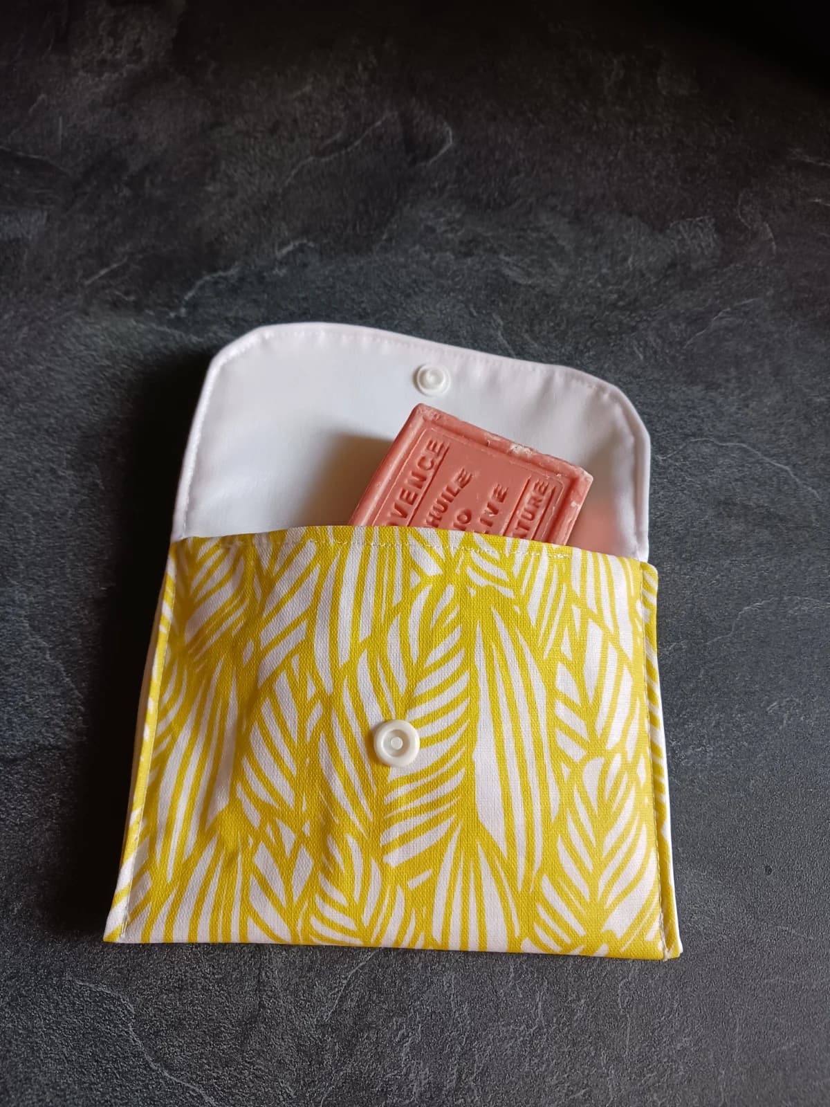 Pochette ouverte en tissu à motifs de feuilles jaunes et blanches, contenant un savon solide rose.