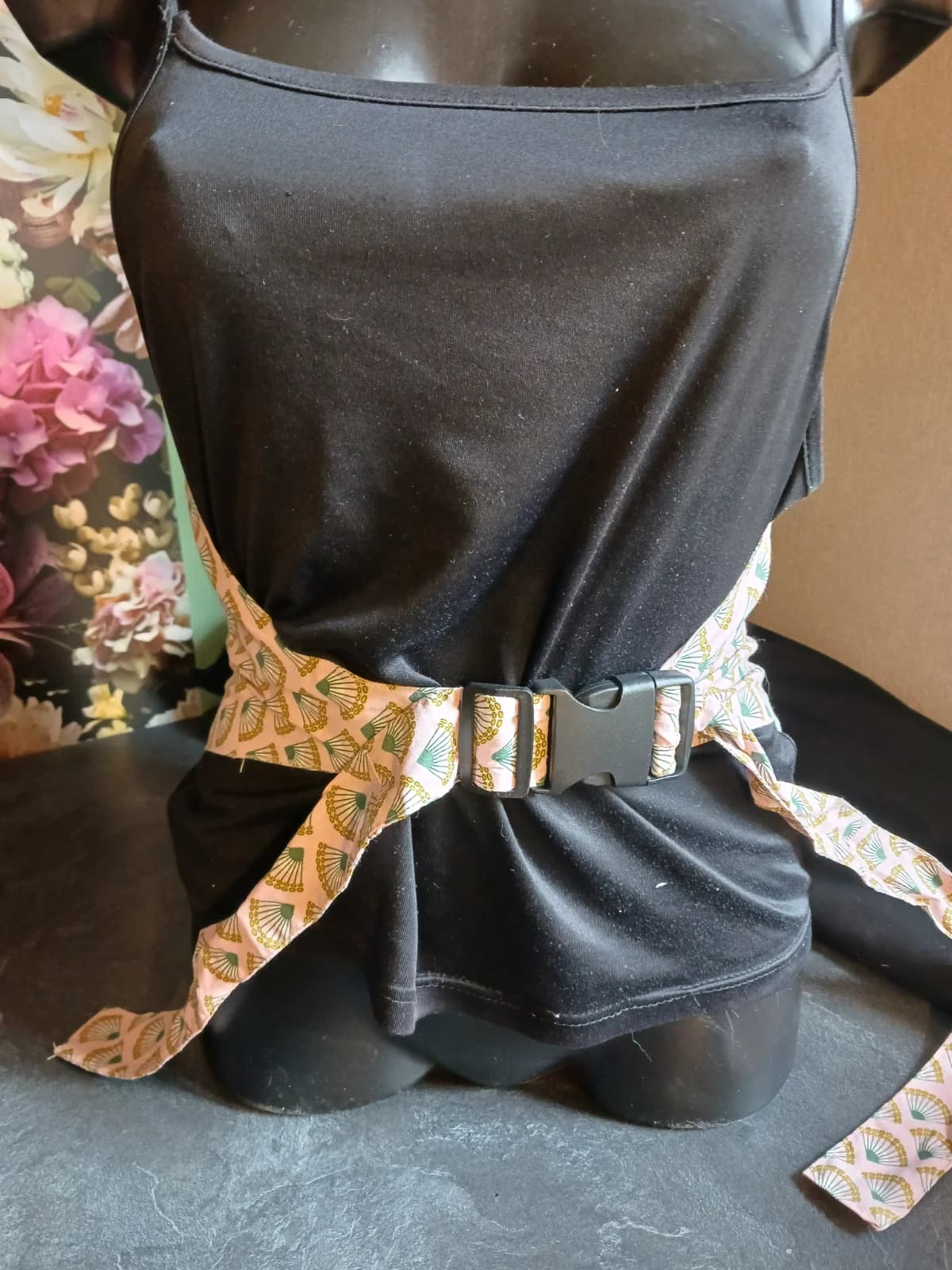 Ceinture bouillotte à motif éventails rose et vert attachée par une boucle noire sur un buste de mannequin.